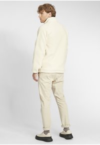 Cream fleece jacket with high collar, paired with light beige chinos and shoes. The jacket features a textured fabric.