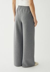 Szürke, bő szárú melegítőnadrág puha anyagból, rugalmas derekú, laza szabással, hátulról nézve bemutatva.