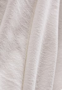 Weißer, strukturierter Stoff fällt sanft und zeichnet sich durch eine plüschige, leicht erhabene Oberfläche und ein glattes, gleichmäßiges Finish aus. Ein dezenter Glanz verbessert sein Erscheinungsbild.