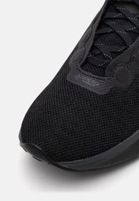 Svart sneakers med et teksturert mesh-parti, som har GORE-TEX-merke, gummisåle og et strømlinjeformet design. Snøringene er mørke og integrert i overdelen.