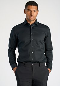 Zwarte long-sleeve shirt met een klassieke kraag en sluiting met knopen aan de voorkant. Gladde stof met zilveren knoopaccenten, gecombineerd met donkere broek.