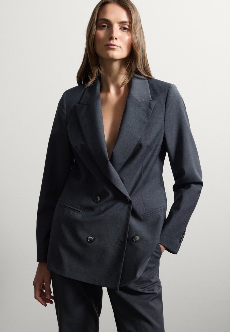 Blazer grigio scuro doppiopetto in tessuto lavorato, con grandi bottoni, rever a punta e una vestibilità ampia. Sono presenti tasche.