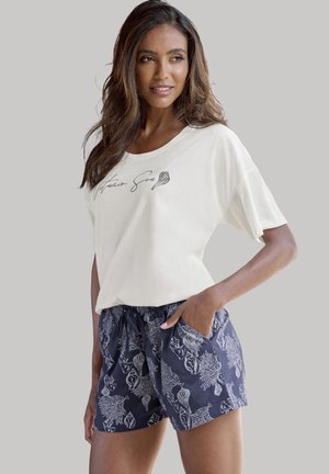 Cremiges oversized T-Shirt mit "Maintain Sea" Grafik, kombiniert mit navyblauen Shorts, die ein Korallen- und Muschel-Muster aufweisen, einen elastischen Bund haben und Taschen besitzen.