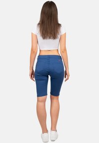 Bermuda shorts in denim blu con un design fitted, tasche frontali e posteriori, e una leggera elasticità. Abbinati a un top corto bianco e sneakers.