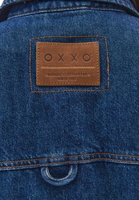 Denimjacka bak med brun läderpatch som läser "OXXO Authentic Denimwear Since 1993" och orange kontrastsöm.