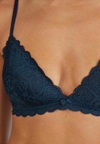 Mariene kant bralette met een diepe V-hals, gegolfde randen, bloemenpatronen, verstelbare bandjes en een centrale strikdetail.