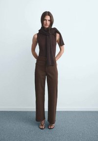 Top marrón sin mangas, pantalones de pierna ancha marrones y una bufanda de punto oscura. Textura suave con sandalias de tiras. Fondo neutro.