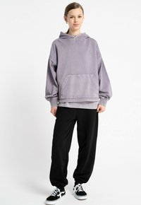 Przesadny fioletowy hoodie z przednią kieszenią, ribbed cuffs i dolnym wykończeniem; zestawiony z czarnymi spodniami dresowymi i czarnymi sneakersami.