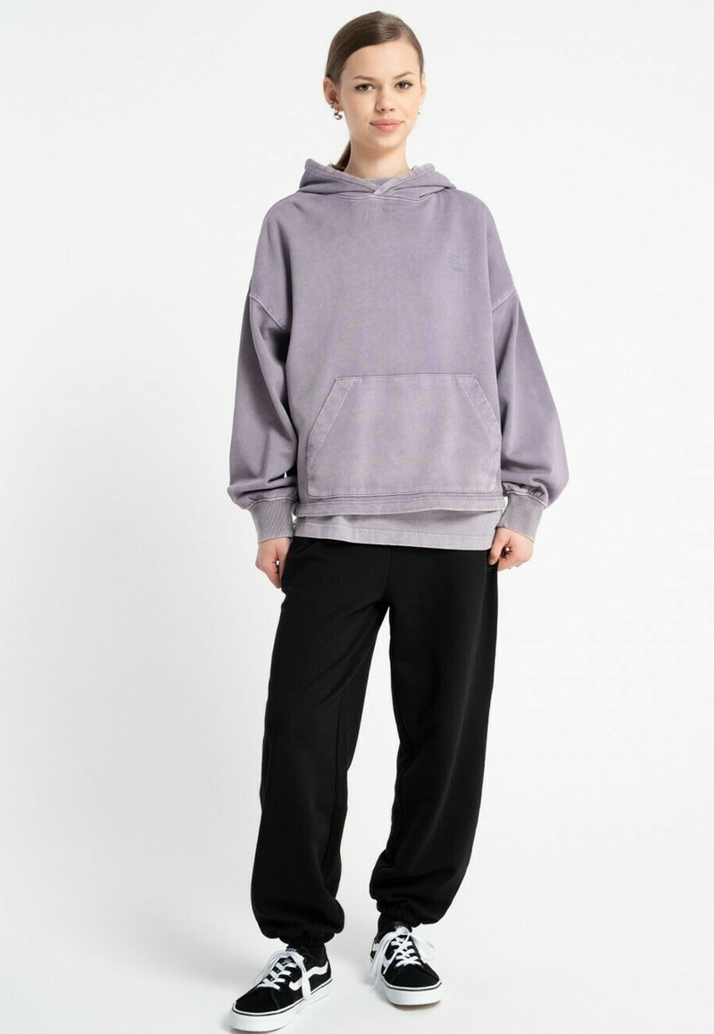 Przesadny fioletowy hoodie z przednią kieszenią, ribbed cuffs i dolnym wykończeniem; zestawiony z czarnymi spodniami dresowymi i czarnymi sneakersami.