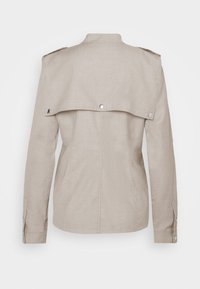 Veste beige à manches longues avec épaulettes, pièce d’empiècement dos et poignets boutonnés, vue de dos sur un fond neutre.