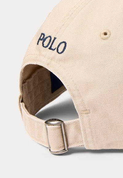 Beige stoff baseballcaps med justerbar metallspenne og blå brodert "POLO" tekst på baksiden.