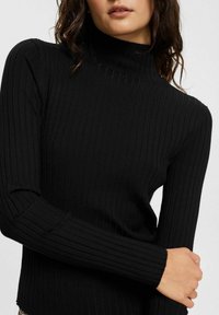 Czarny prążkowany sweter z golfem i długimi rękawami, o dopasowanym kroju i miękkiej fakturze. Zbliżenie na szczegóły tkaniny i sylwetkę.