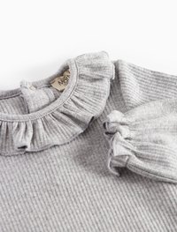 Svetlo sivo rebrasto pleteno majico za dojenčke z nabrano ovratnikom in manšetami, ki ima pritisne gumbe na hrbtni strani vratu.