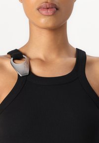 Juodas banguotas tank top'as su apvaliu iškirpimu ir metaliniu segtuku ant peties dirželio. Lygi tekstūra, prigludusi forma.