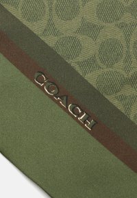 Green fabric featuring a tonal logo pattern, a dark brown stripe, and embossed "COACH" text. Smooth texture, rectangular shape.
