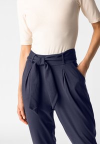 Marinblå högmidjade byxor med knytbälte, med veck och sidfickor. Lättviktsmaterial med en jämn textur.