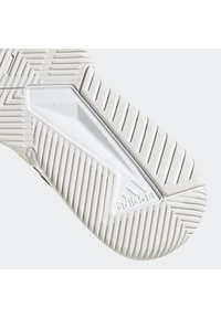 Semelle blanche texturée d'une chaussure Adidas avec des rainures diagonales et une section triangulaire transparente près du talon affichant le logo Adidas.