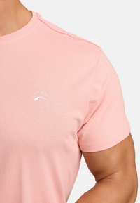 Light pink cotton t-shirt with a round neckline, short sleeves, and a small white logo featuring "EST. 1993" on the chest.