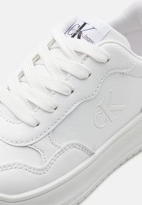 Sneaker bianca in pelle con superficie testurizzata, lacci spessi e logo ‘cK’ stampato di lato. Presenta una suola imbottita e una finitura liscia.