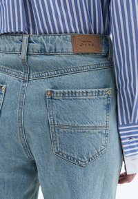 Ljusblå denimjeans med hög midja, med två bakfickor, synlig sömnad och en lädermärke på midjebandet.