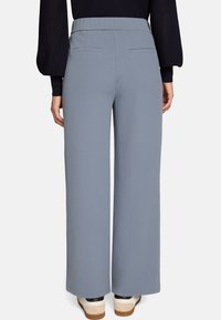 Pantalon large bleu clair avec une texture lisse et une taille haute, doté de deux poches arrière et associé à des baskets blanches et noires.