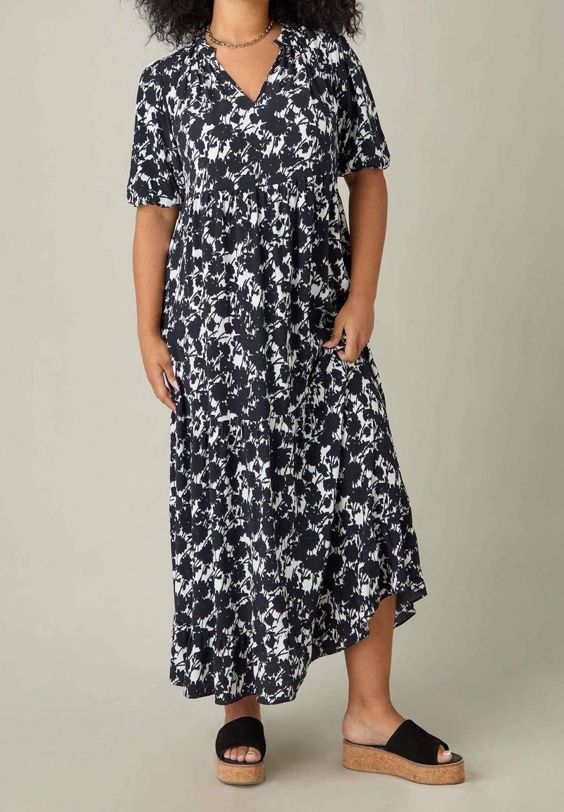 Maxiklänning i marinblått med vitt blommönster, korta puffärmar och V-ringning. Har en lager-på-lager nederkant och fickor. Kommer tillsammans med svarta platåsandaler.