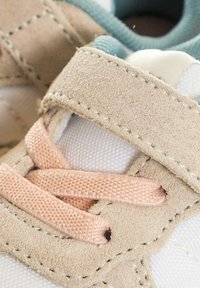 Sneaker bianca con accenti in suede beige, dotata di lacci rosa e di una fodera interna azzurro chiaro. I dettagli includono cuciture attorno alla suola.
