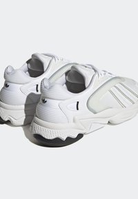 Vita sportskor med texturerat tyg, släta detaljer, tjock gummisula och tydliga lagerförsedda designelement.