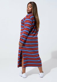 Długa sukienka w paski z czerwonymi i niebieskimi poziomymi paskami, wykonana z miękkiego materiału; zawiera boczne rozcięcie dla zwiększenia stylu.