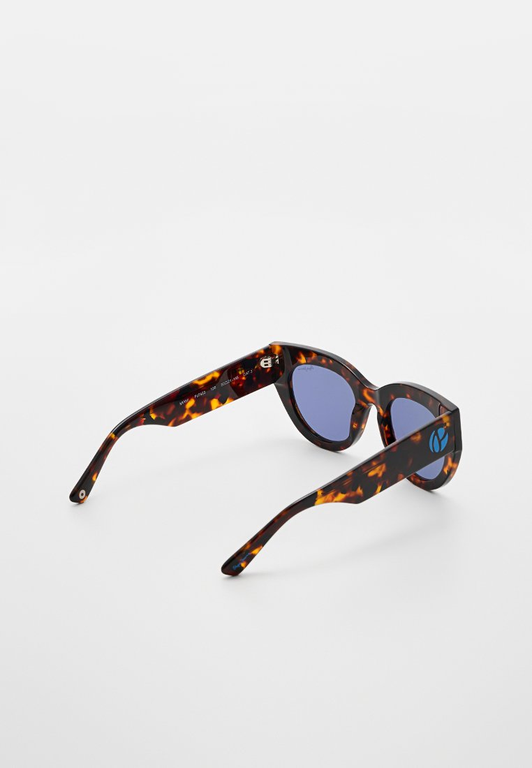 Sonnenbrille mit Schildpatt-Rahmen und blauen Gläsern, auf einer weißen Fläche präsentiert, um das Innenteil des Bügels und das Logo an der Seite zu zeigen.
