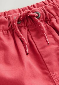 Shorts rossi con coulisse realizzati in tessuto morbido, dotati di una coulisse intrecciata con occhielli in metallo per la regolazione e dettagli di cucitura.