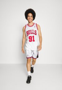 Tricou de baschet alb cu accente roșii și inscripția "BULLS 91"; asortat cu pantaloni scurți albi cu un model alb și roșu; pantofi negri.
