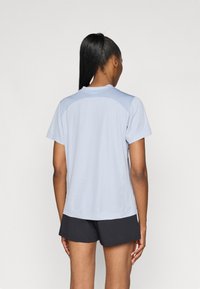Ανοιχτό μπλε αθλητικό μπλουζάκι με κοντά μανίκια, στρογγυλή λαιμόκοψη και υφασμάτινες λεπτομέρειες στους ώμους. Συνδυασμένο με μαύρες βερμούδες, προσφέροντας μια casual εμφάνιση.