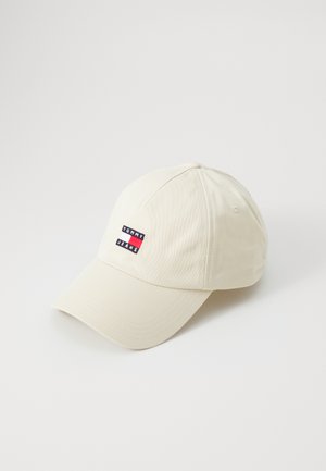 Casquette crème avec une visière incurvée, arborant un logo rectangulaire brodé en rouge, blanc et bleu portant l'inscription "TOMMY JEANS." Matériau en coton.