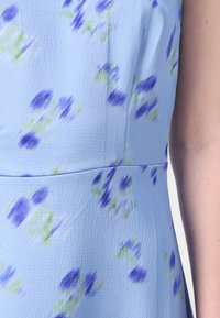 Light blue dress featuring a textured fabric with a floral pattern in purple and green. Includes seams and a fitted bodice design.