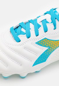 Scarpino da calcio bianco con lacci e dettagli turchesi, caratterizzato da un motivo geometrico blu e oro, parte superiore texturizzata e tacchetti moldati.