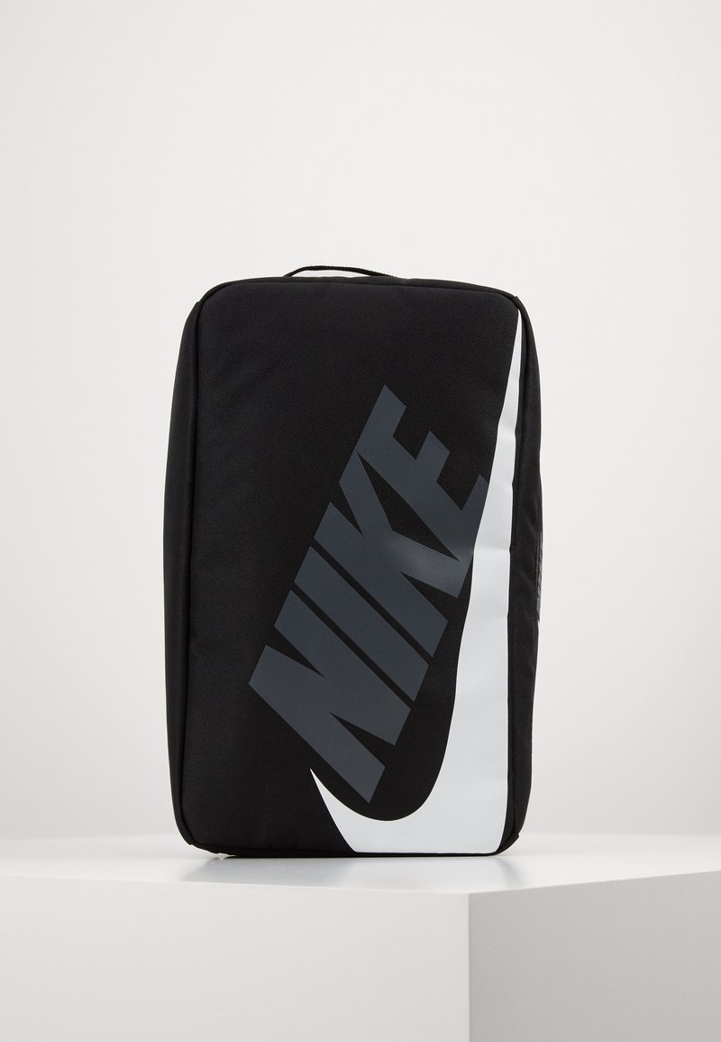 Svart rektangulär Nike-väska med stor vit swoosh-logotyp och mörk "NIKE"-text, stående upprätt på en vit yta mot en enfärgad bakgrund.
