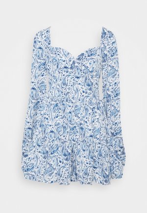 Robe courte à manches longues et à volants, imprimé cachemire bleu et floral, décolleté en cœur et épaules bouffantes sur fond blanc.