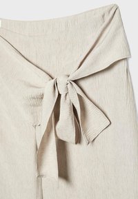 Pantalon en tissu texturé beige avec une taille haute et une large ceinture nouée en un nœud papillon à l'avant.