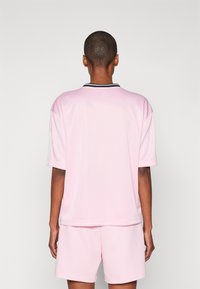 Jersey atlético rosa de manga corta, con cuello redondo y ribetes negros. Combinado con pantalones cortos a juego, que presentan una textura suave y un corte relajado.