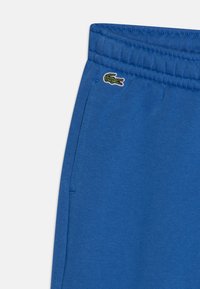 Pantalon de jogging en coton bleu avec une taille élastique et un petit logo crocodile brodé en vert. Comprend des poches latérales.