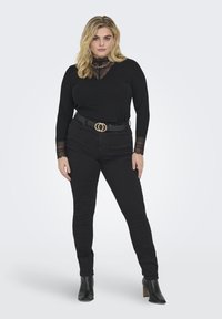 Black long-sleeve top with lace detailing at the neckline and cuffs, paired with black skinny jeans and a gold-ringed black belt.