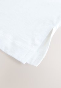 T-shirt in cotone bianco con una texture morbida, caratterizzato da spacco laterale all'orlo e cuciture doppie per una maggiore durata.