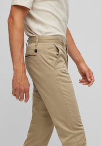 Khaki chinos i lättviktsmaterial, med sidofickor, en bakficka med etikett och en slim fit-design.