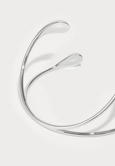 Bracelet en métal argenté avec des extrémités lisses et courbées. Fini poli, design minimaliste, sans motifs ni accents visibles.