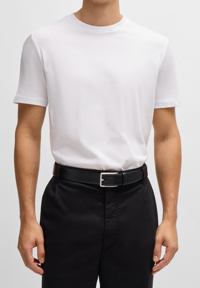 Biała bawełniana koszulka w połączeniu z czarnym skórzanym paskiem z prostokątną srebrną klamrą, noszona z ciemnymi spodniami.