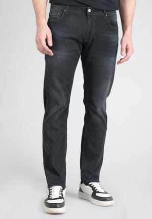 Zwarte denimjeans met een slim fit, voorzien van vijf zakken en lichte vervaging. Gecombineerd met zwart-witte sneakers.