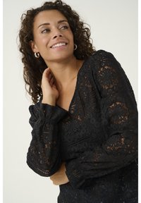 Top in pizzo nero con scollatura a V e maniche lunghe a sbuffo, caratterizzato da intricati motivi floreali e dettagli testurizzati in tutto il capo.