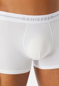 Vita bomullsboxer med en mjuk elastisk midjeband som har "SCHIESSER"-logotypen. Slät textur, åtsittande design, längd till mitten av låret.