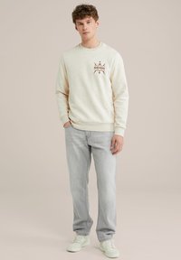 Lichtcreme crewneck sweatshirt met grafische print, gecombineerd met lichtgrijze jeans en witte sneakers. Soepele stof, relaxed fit.